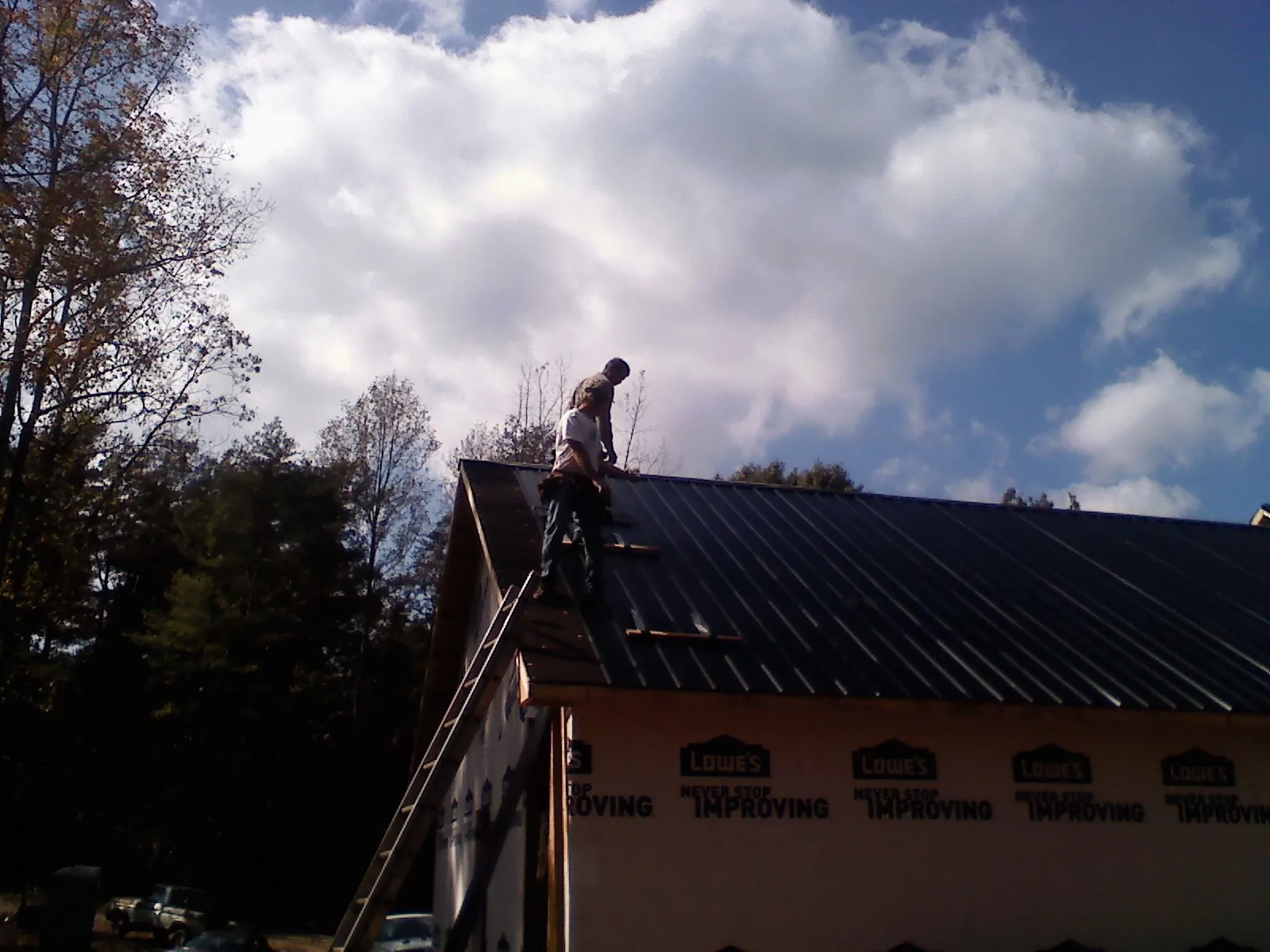 Roofer fastening dark metal panels high against a cloudy sky, from a Roof Inspection job in Middleport